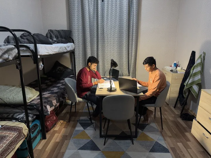 Two students studying with books and laptops in a shared room with bunk beds