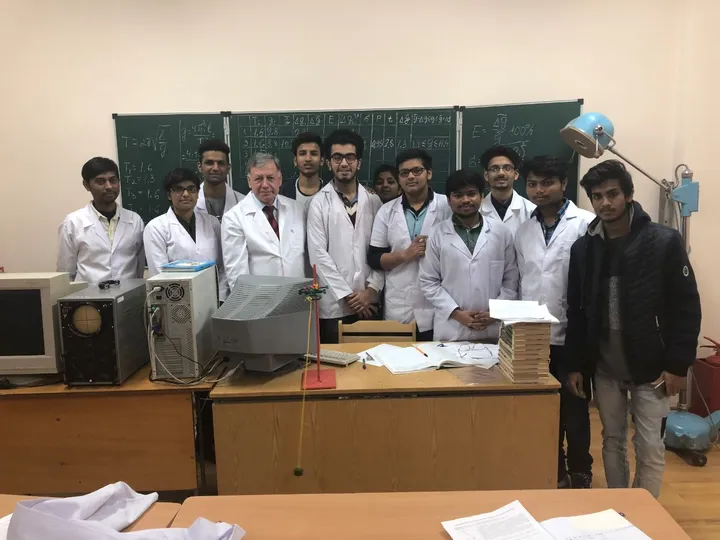 Group in white coats standing beside laboratory equipment and a chalkboard