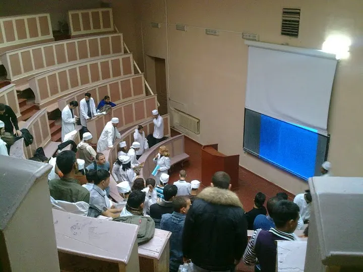 Students in white coats gathered in a tiered lecture hall