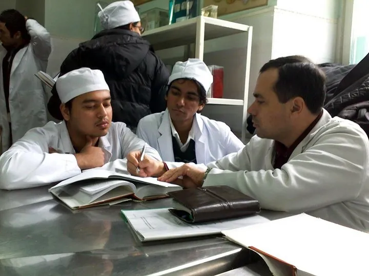 Small group in white coats discussing an open textbook around a desk