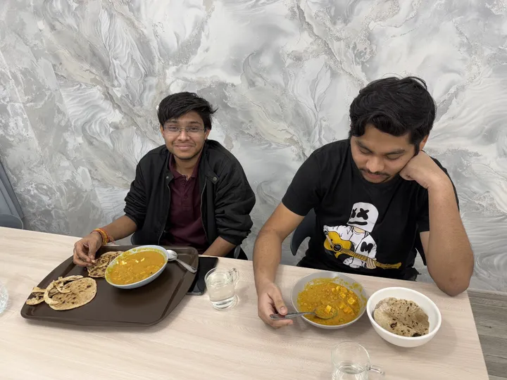 Two students seated at a dining table with flatbreads and curry